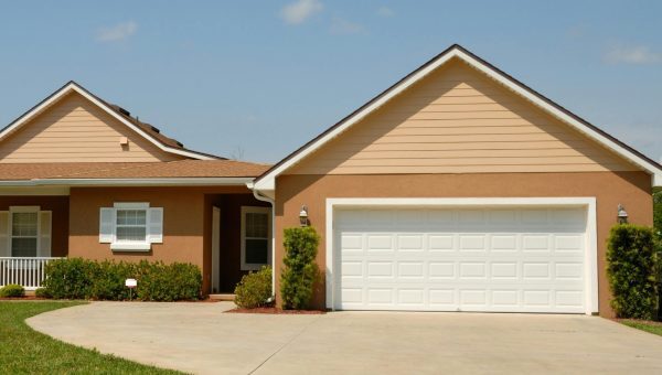 A single-story, tan-colored stucco home with a white, traditional raised panel garage door and brown roof trim.